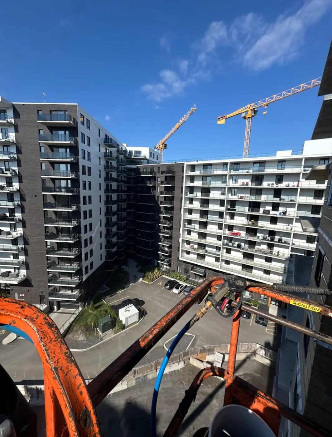 Lance haute pression sur une nacelle, en hauteur devant des tours à condos et des grues